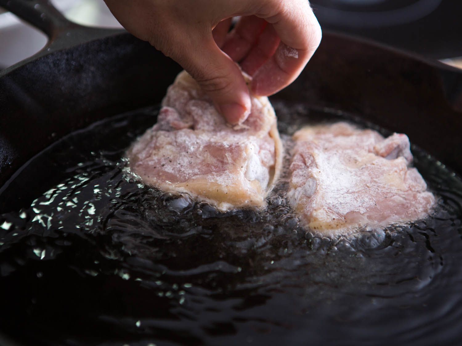 Placing pieces of flour-coated chicken into a pan of hot oil for Maryland fried chicken.