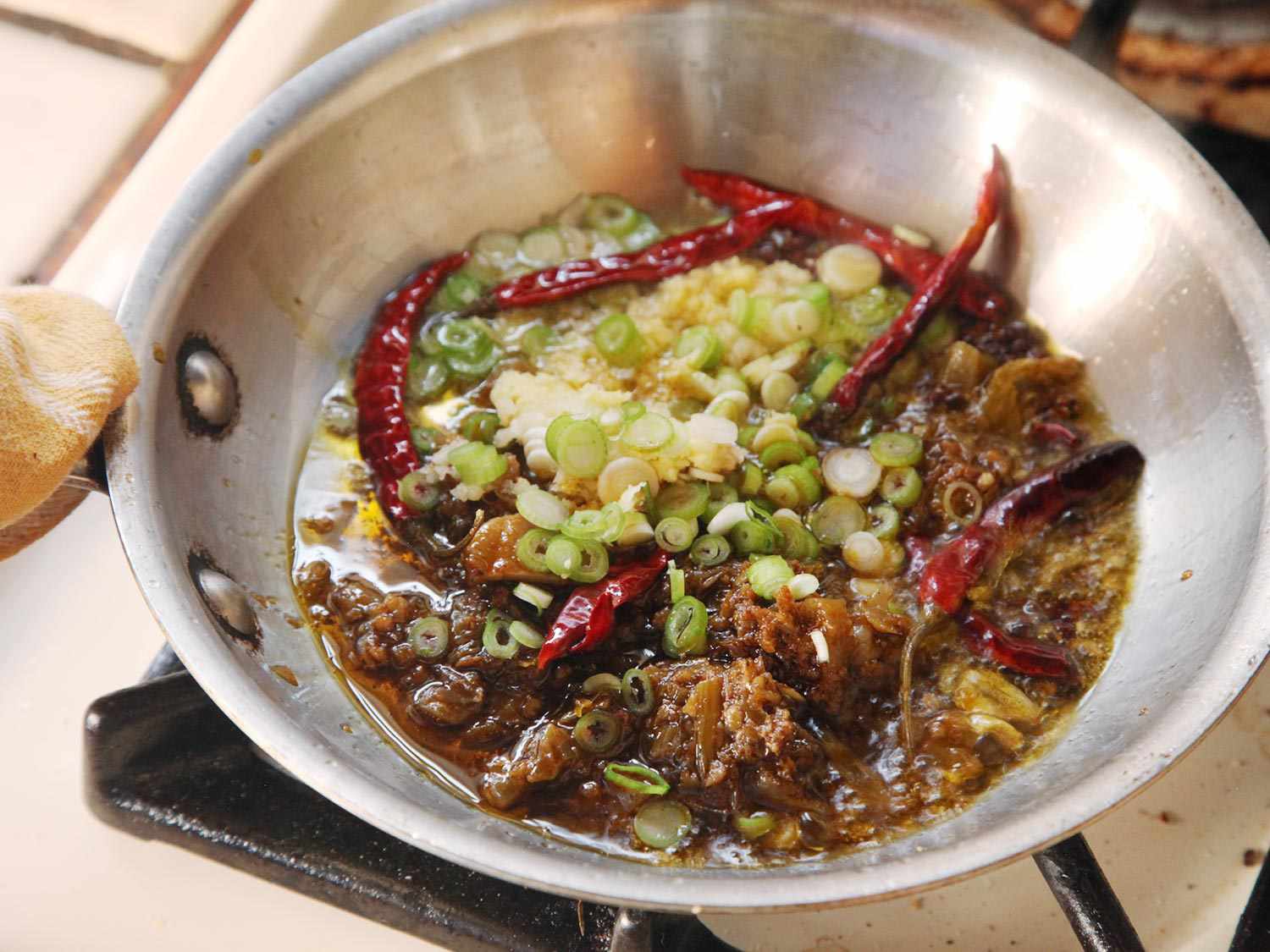 Chiles, Sichuan peppercorns, ginger, garlic, and scallions are gently fried in a small skillet.
