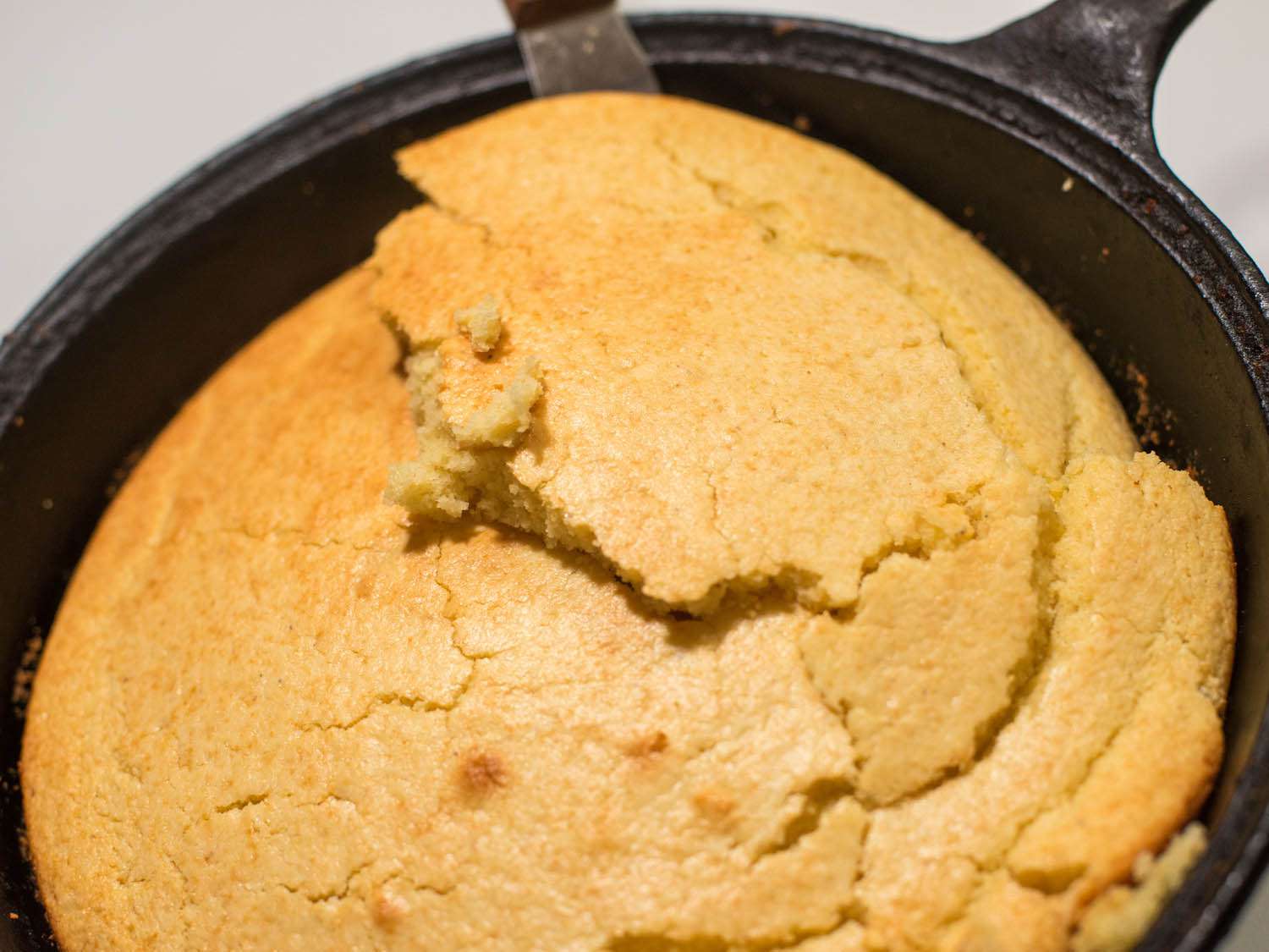 An offset spatula lifting a test batch of too-tender cornbread from a skillet, but it breaks apart.