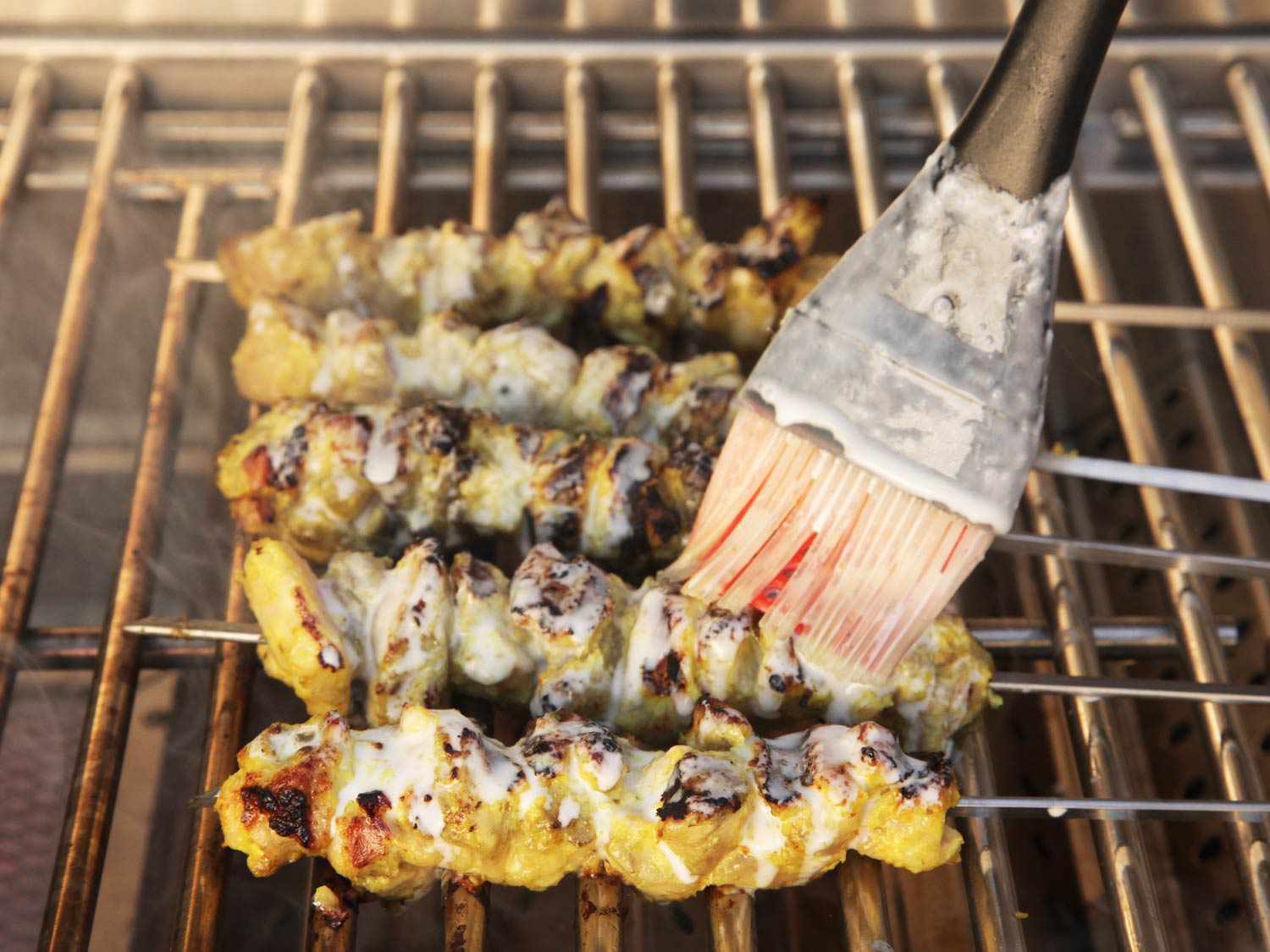 Brushing coconut milk onto chicken satay on the grill. 