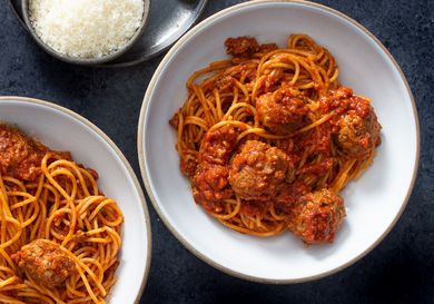 Two bowls of homemade spaghetti and meatballs with a dish of grated parmesan cheese next to them.
