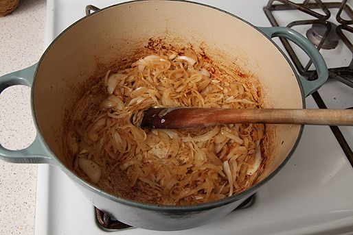 Onions caramelizing in the bottom of an enamel cast iron Dutch oven.