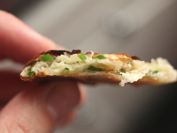 A hand holding a close-up of a torn scallion pancake, showing layers and scallions.