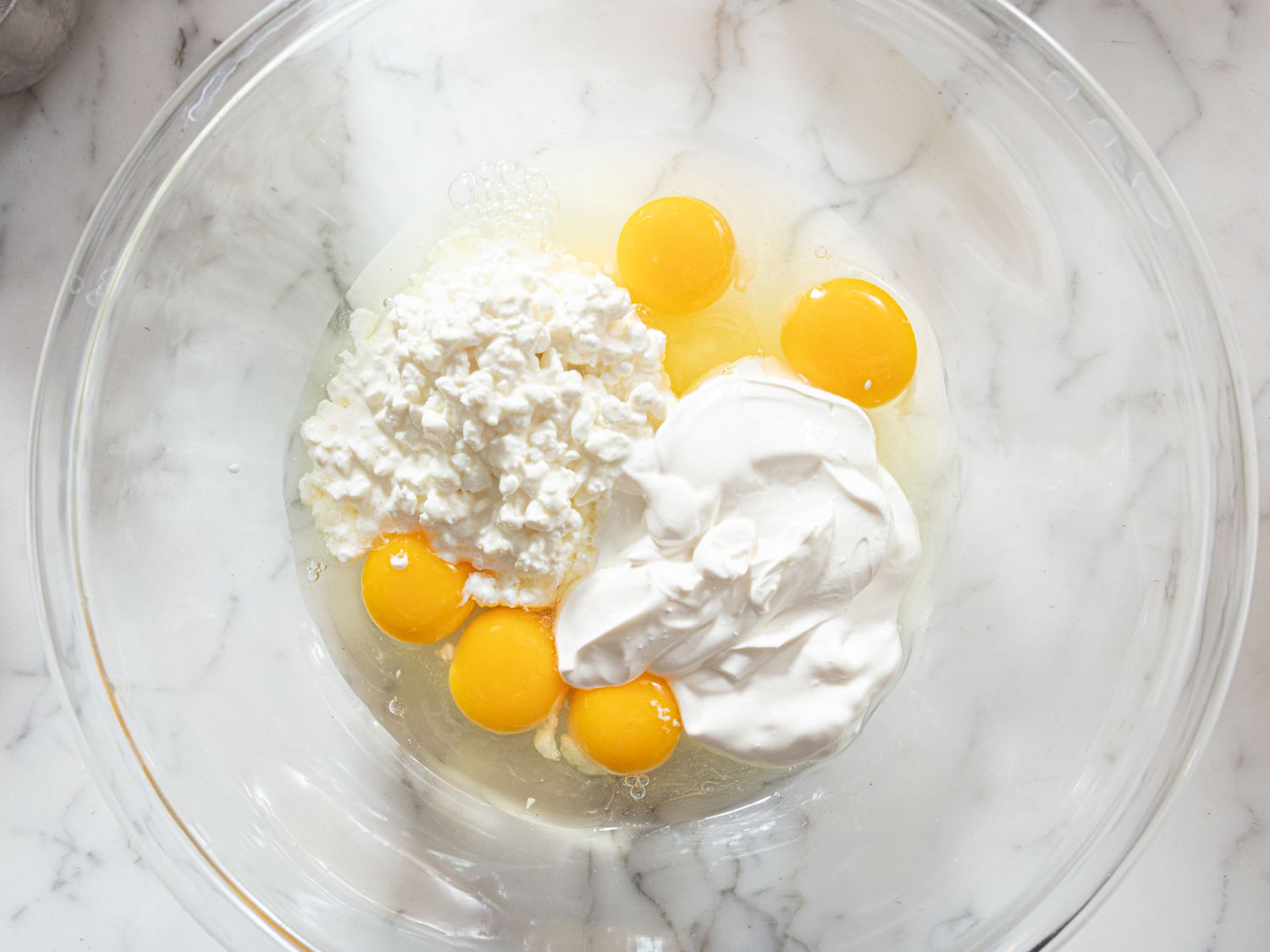 Eggs and ingredients in glass bowl on marble surface. 