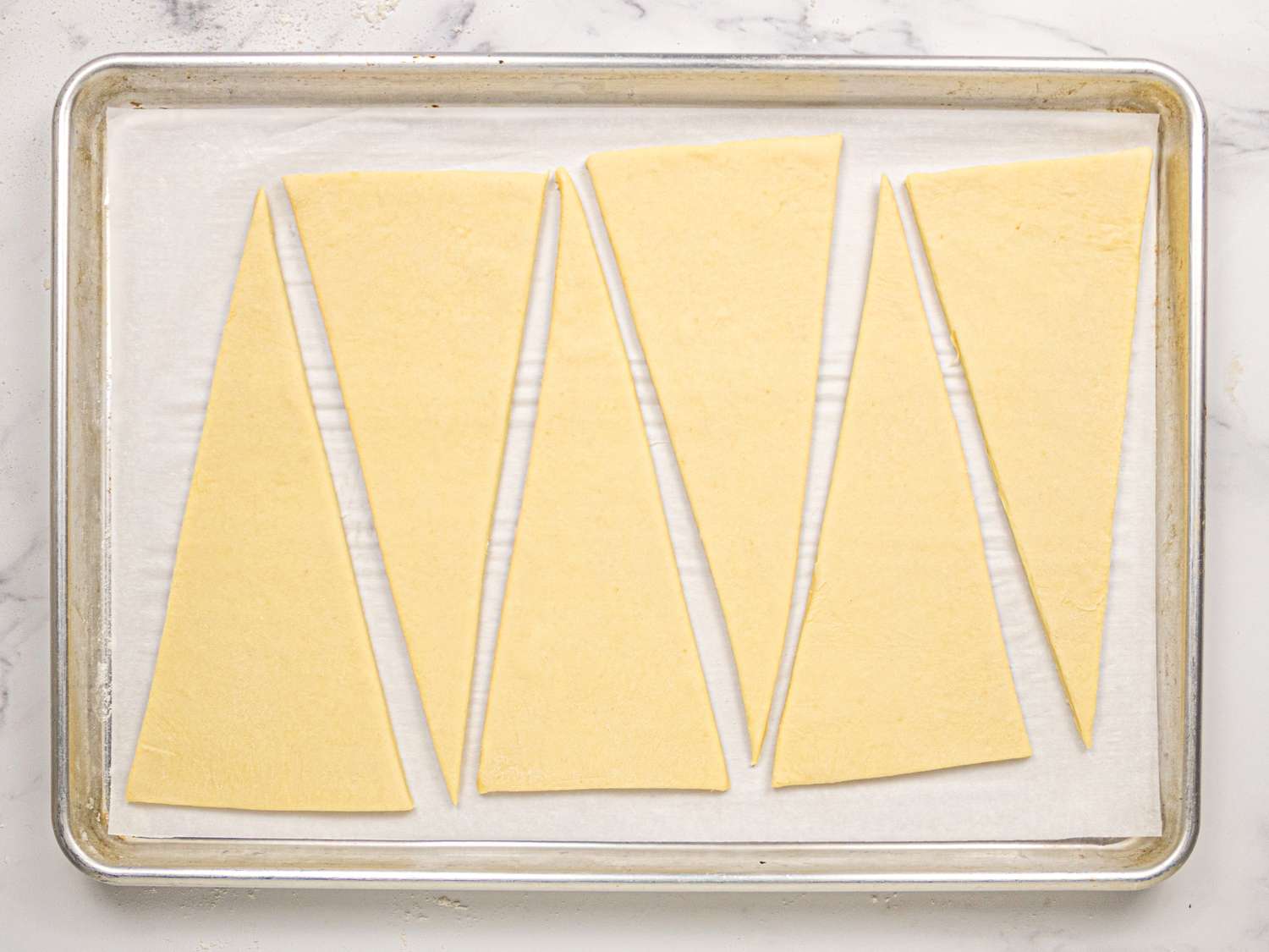 Triangle dough pieces on a baking sheet ready for croissant preparation