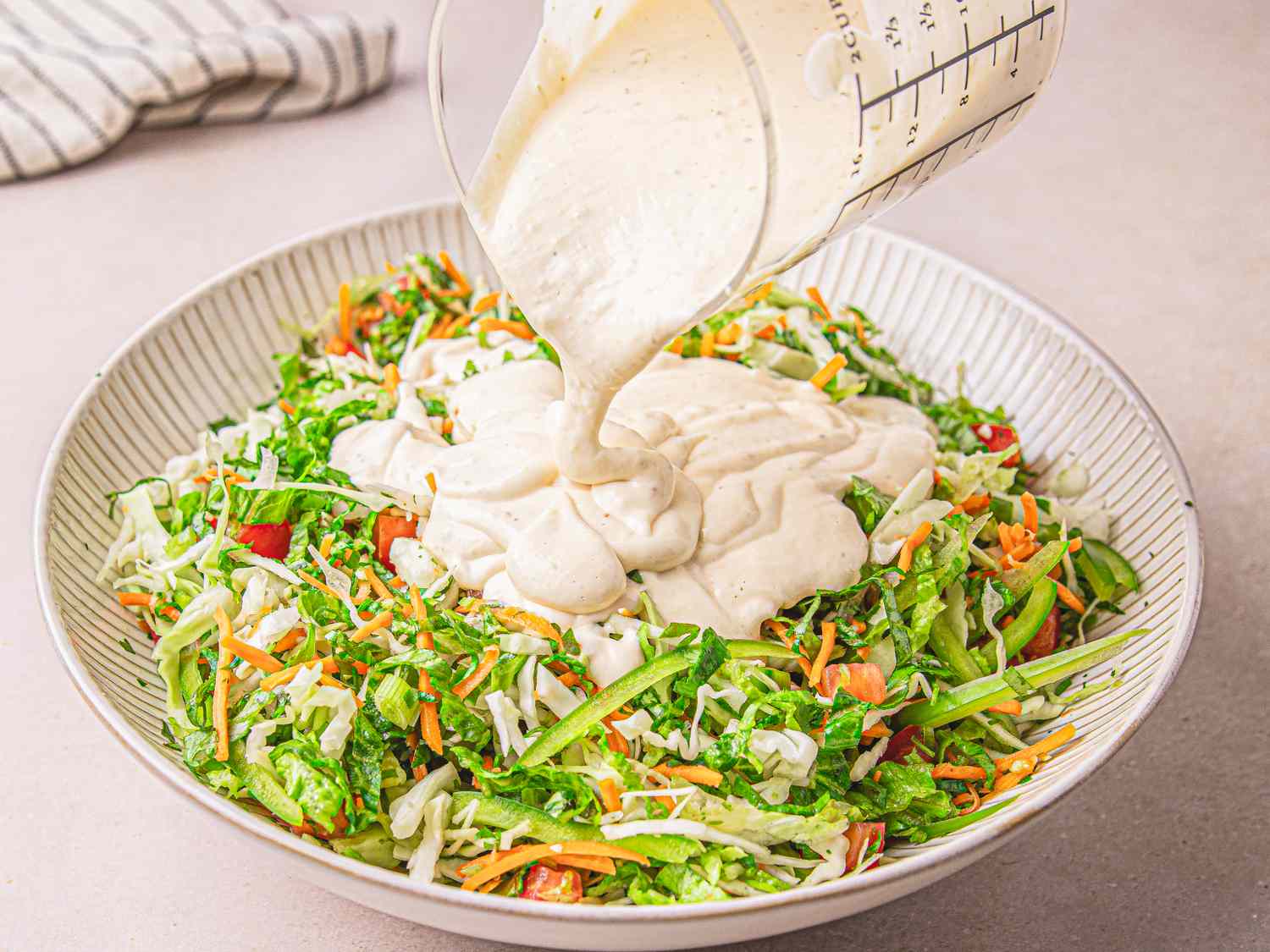 A bowl of salad with shredded vegetables dressing being poured on top