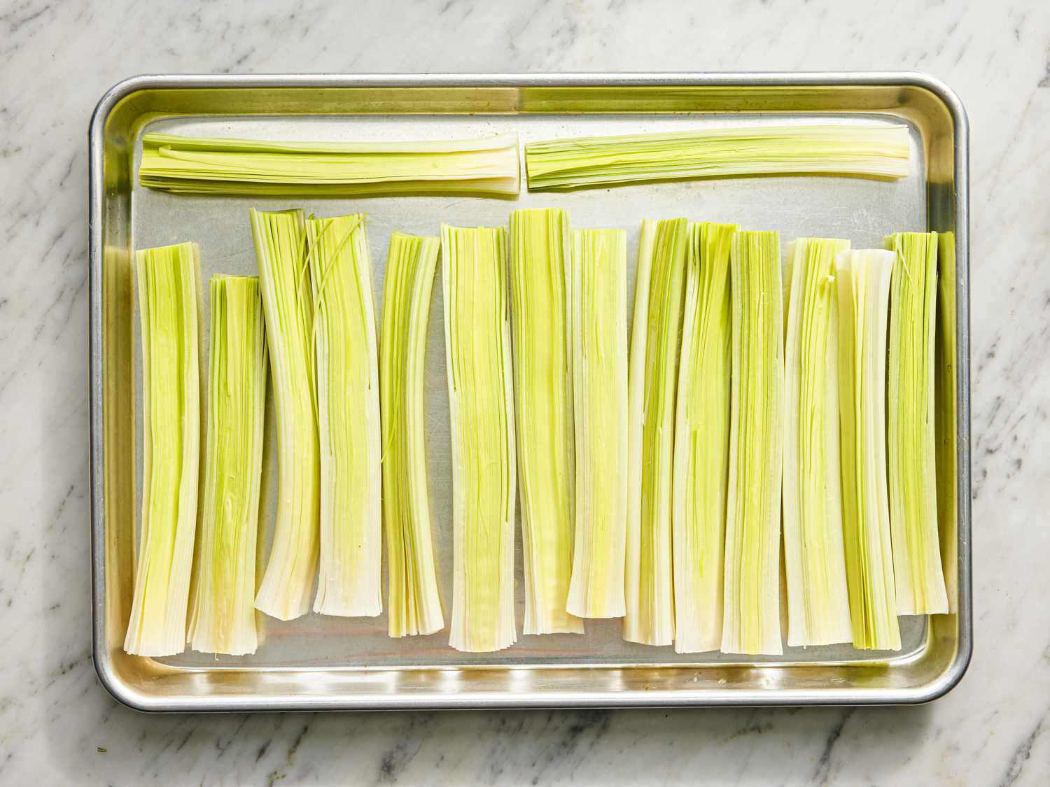 Trimmed leeks spread flat on a baking sheet