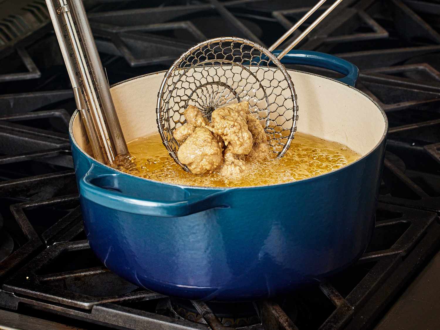 Dipping chicken into dutch oven of heated oil on stove top with slotted spider spoon 