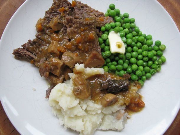 Pot roast on a white plate with buttered peas, mashed potatoes and gravy. 