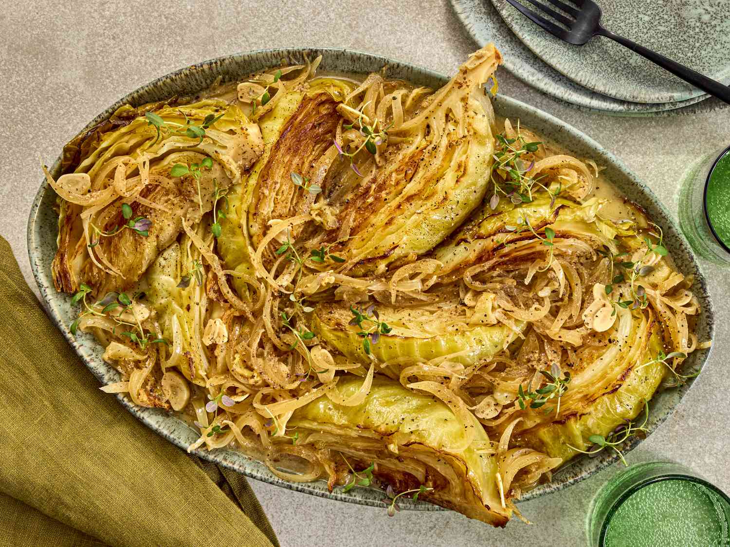 cabbage on a platter with plates, forks and green napkins, and cups on the sides
