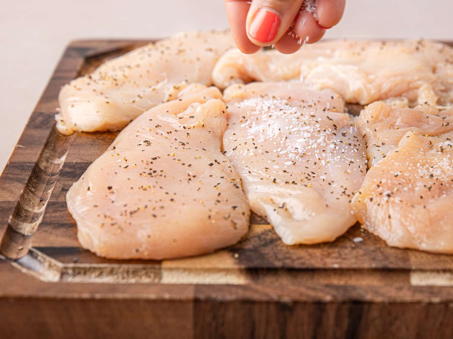 Chicken breasts on a cutting board being sprinkled with seasoning preparation for Chicken Francese