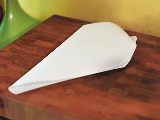 A folded square of parchment paper cut into a half-heart shape laying on a wooden board.