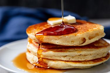 A stack of pancakes topped with butter and syrup being poured over them