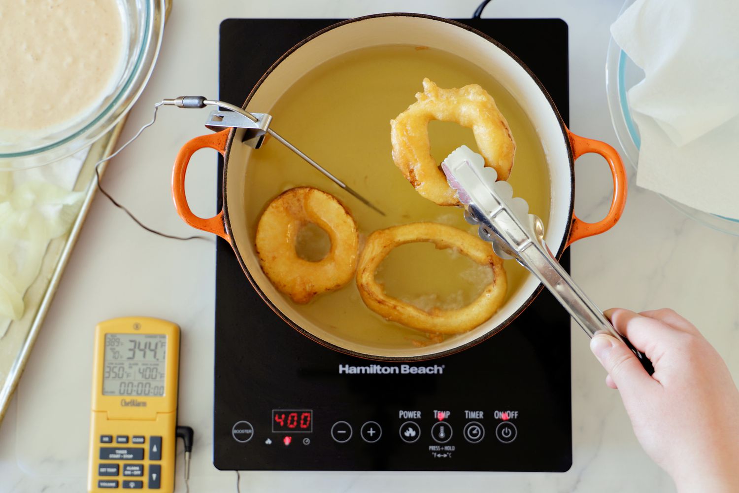 A person using tongs to retrieve a fried donut from frying oil in a Dutch oven set on a portable induction burner.