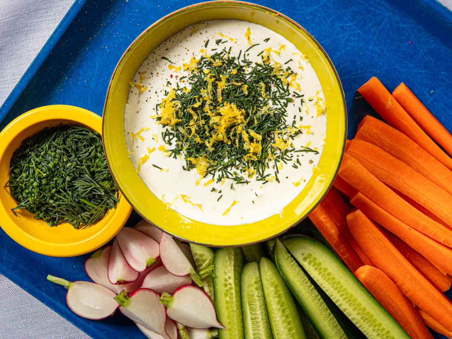 Whipped cottage cheese topped with fresh herbs and lemon zest next to raw vegetables.