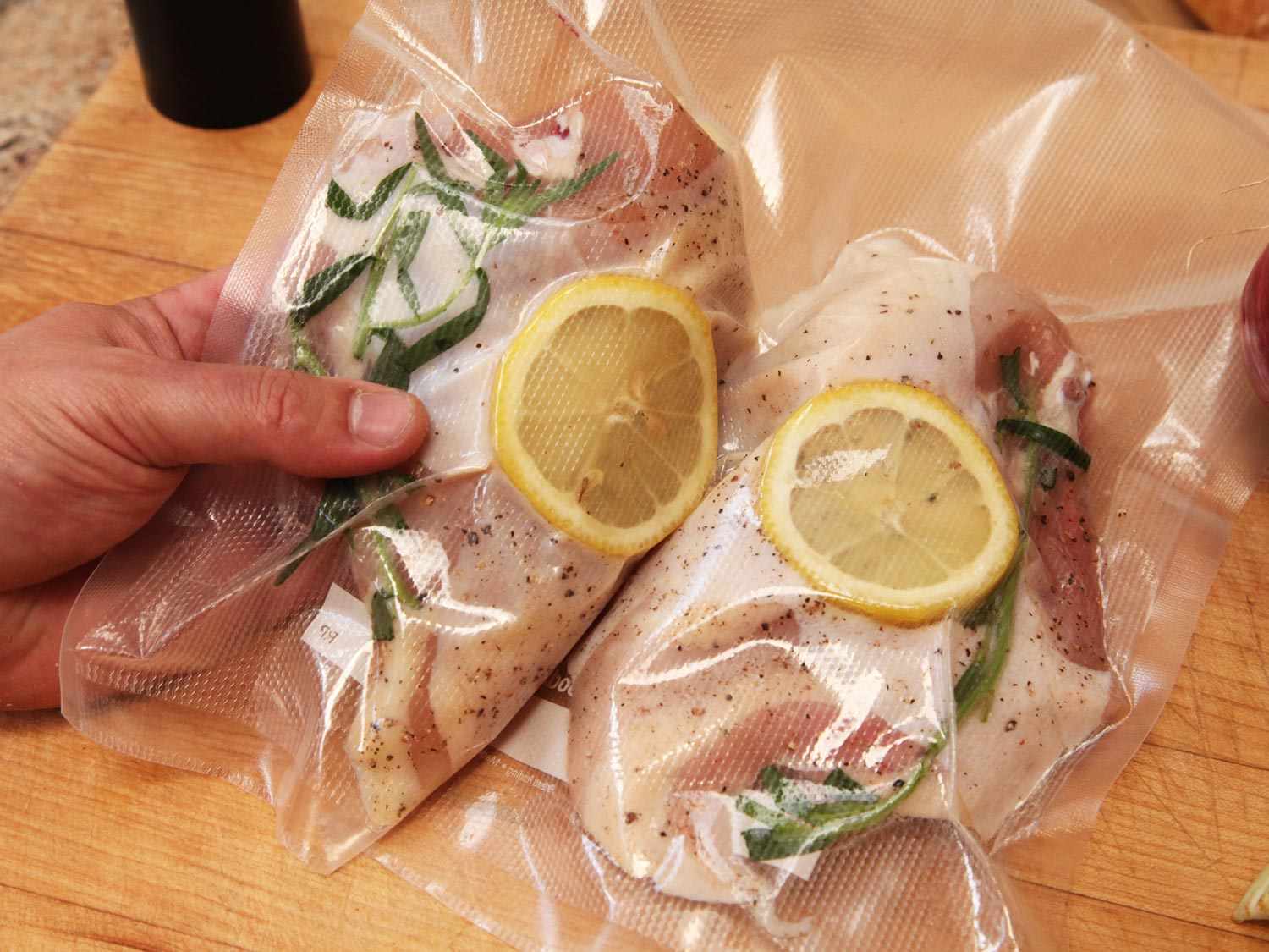 Chicken breasts bagged with lemon slices and herbs for sous vide cooking.
