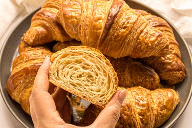 A plate of croissants with a hand holding a halved croissant showing its layers