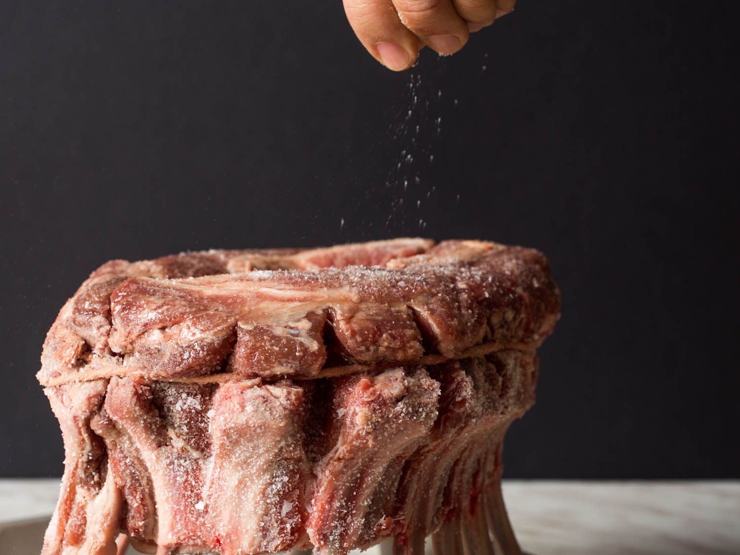Seasoning a crown roast of lamb with salt.
