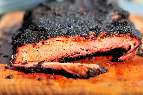 A piece of smoked brisket with a charred crust on a cutting board. 