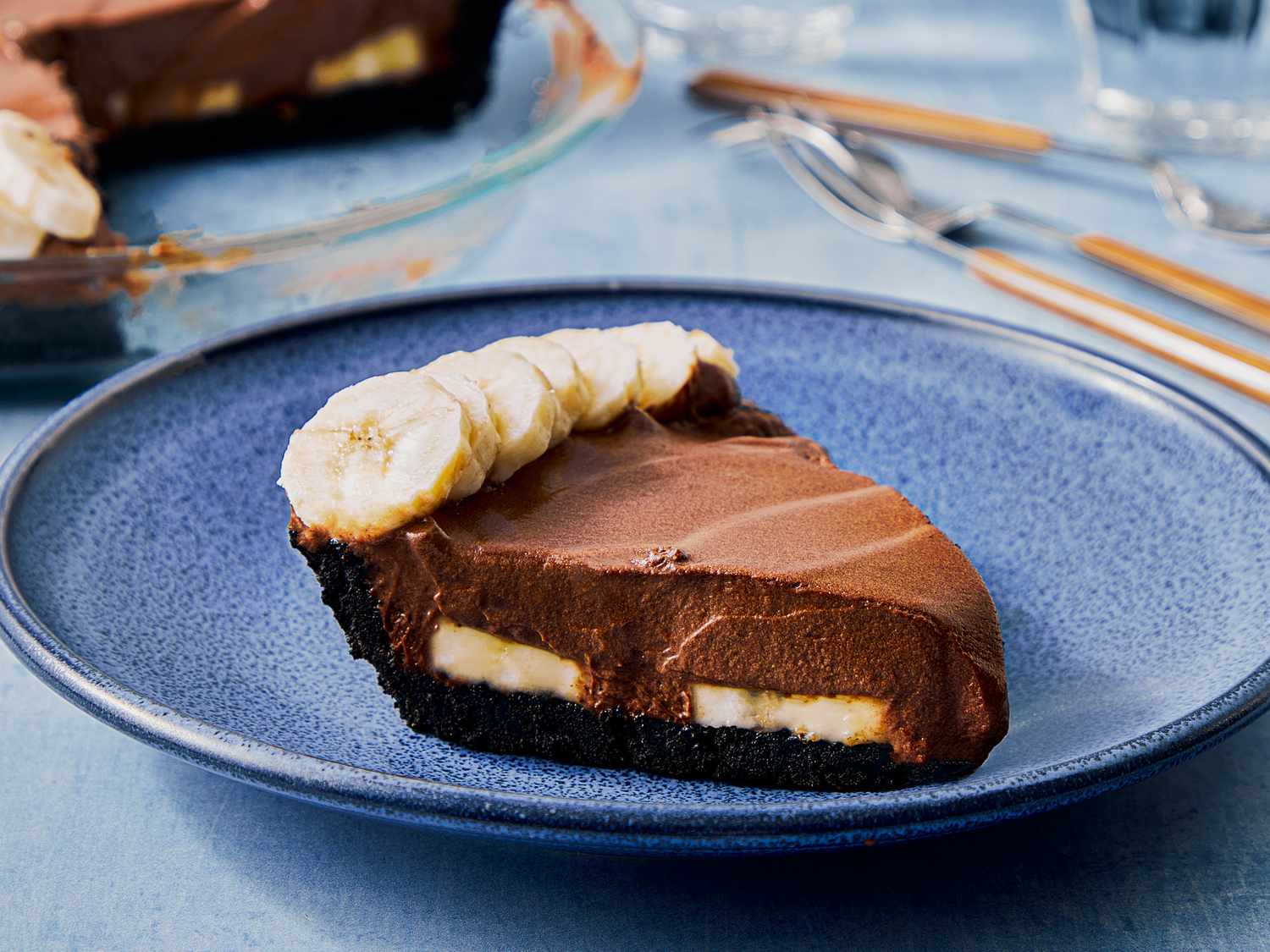 A slice of creamy chocolate banana pie on a blue plate topped with banana slices and a layered filling visible