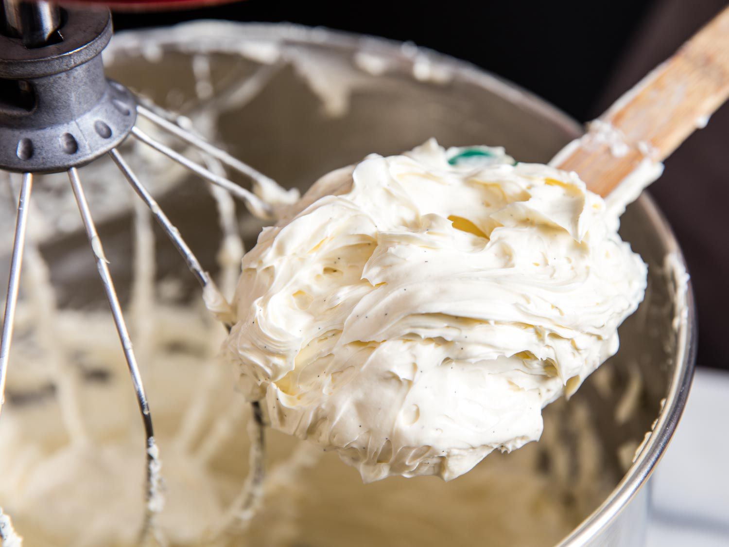 A wooden spoon mounded with buttercream overlooking the bowl of a stand mixer.