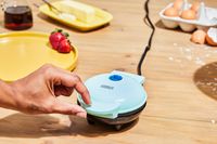 A Dash mini waffle maker in use on a cluttered countertop