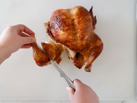 A person using a boning knife to carving a roasted chicken.