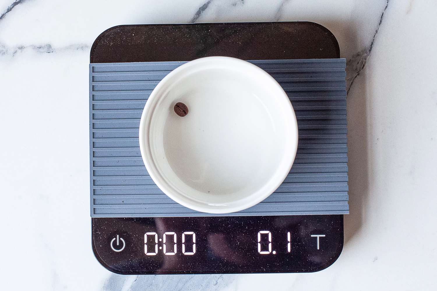 A coffee bean in a small white bowl placed on Acaia Pearl showing 0.1 grams