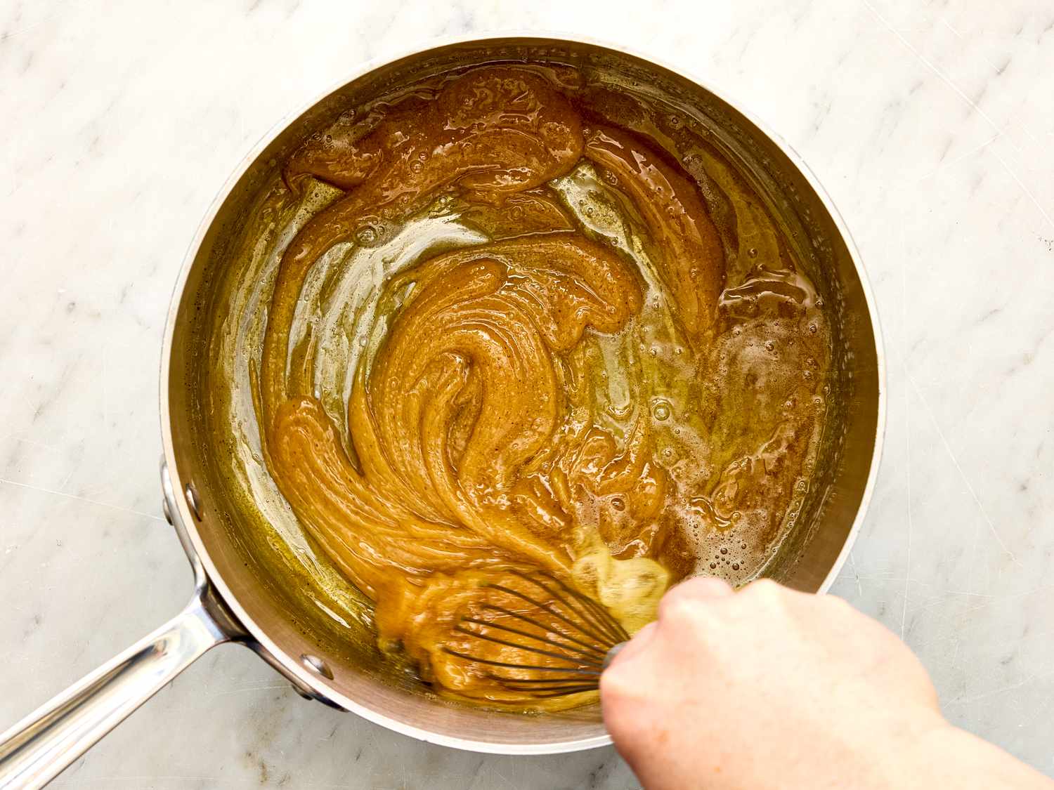 A persons hand whisking a mixture in a saucepan creating a smooth consistency