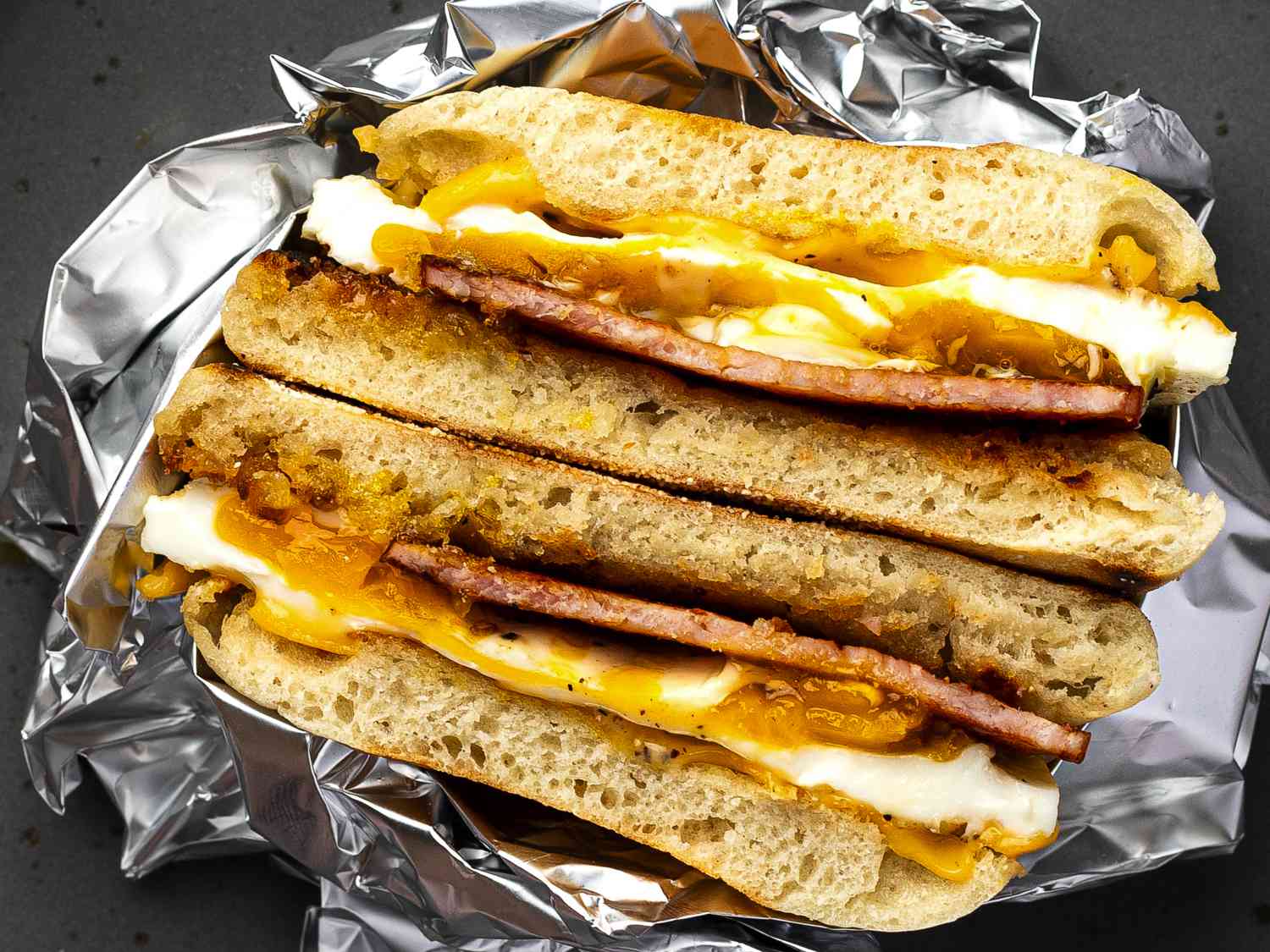 A cooked homemade Egg McMuffin, split in half and wrapped in aluminum foil.