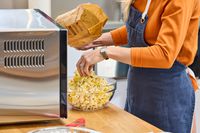 A person emptying a package of popcorn next to the Panasonic - 2.2 Cu. Ft. 1250 Watt SD987SA Full-Size Microwave with Inverter