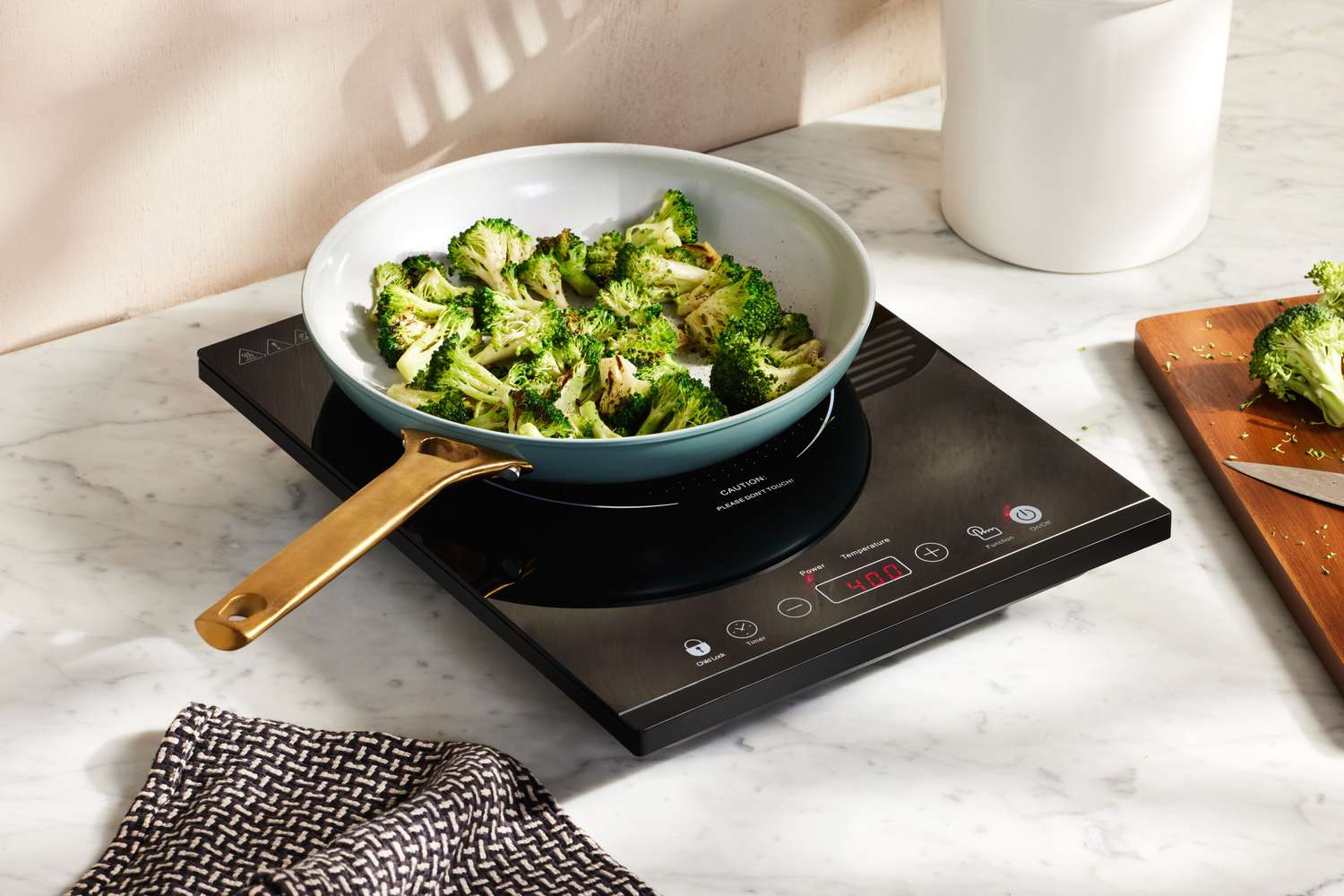 A ceramic pan filled with broccoli atop an induction burner.