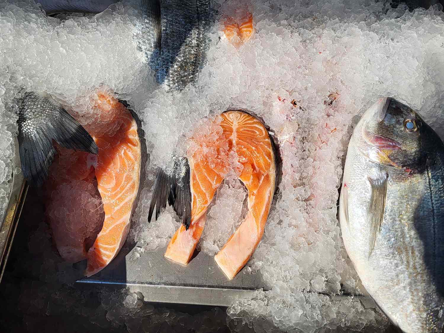 Fish fillets and whole fish on ice display at a market