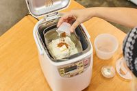 A hand adding ingredients into the Zojirushi Home Bakery Mini Breadmaker