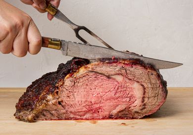 A cooked prime rib roast being carved with a knife and fork on a cutting board
