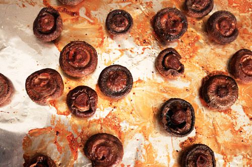 Whole roasted mushrooms on a sheet of aluminum foil stained with mushroom drippings.