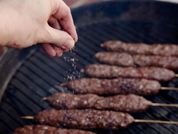 Author sprinkling kebabs on the grill with the salt-cumin-sumac mixture.