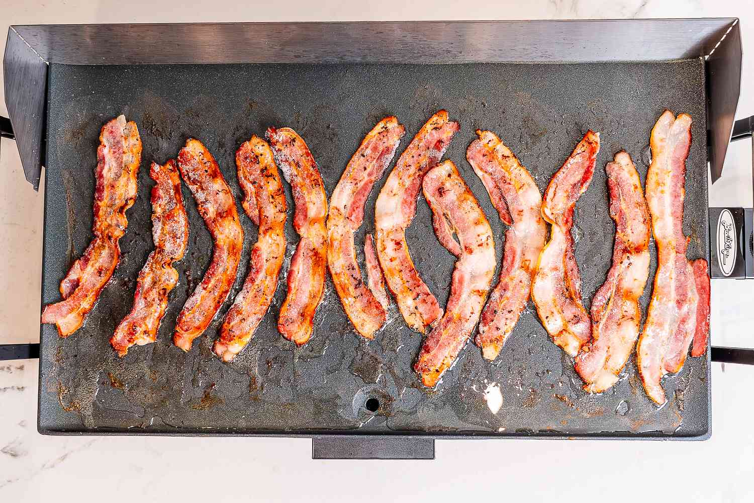 Several strips of bacon cooking on an electric griddle