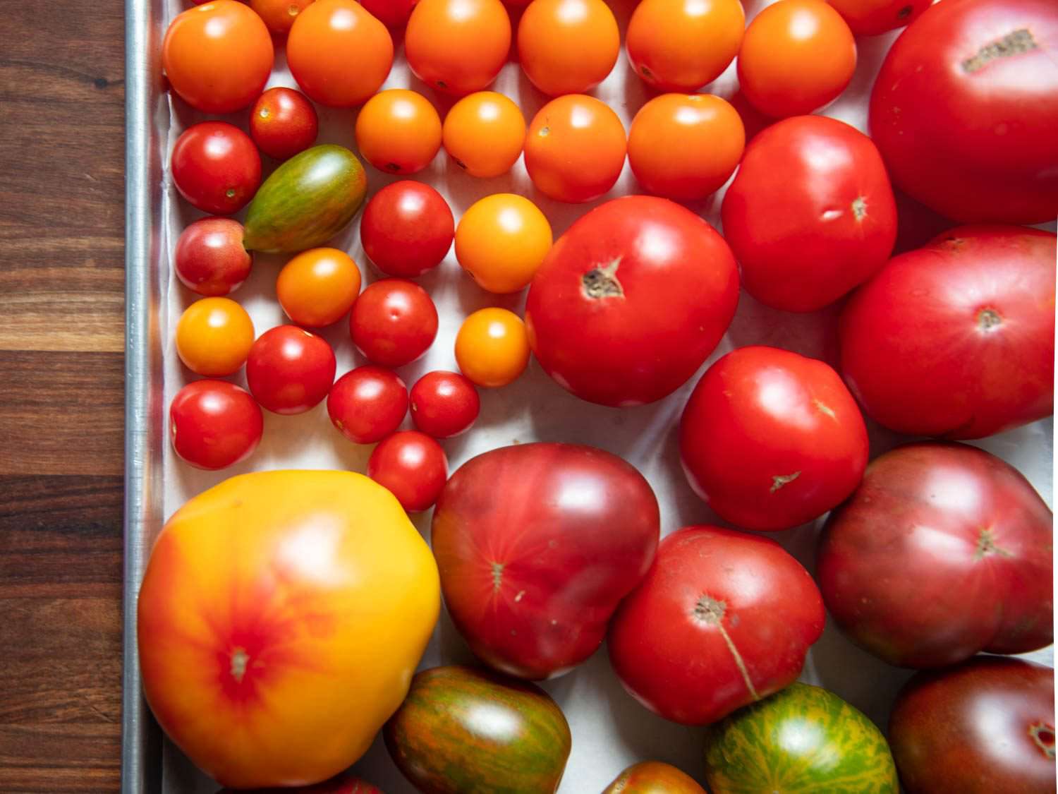 Closeup overhead of a sheet pan full of tomatoes of different colors and sizes.
