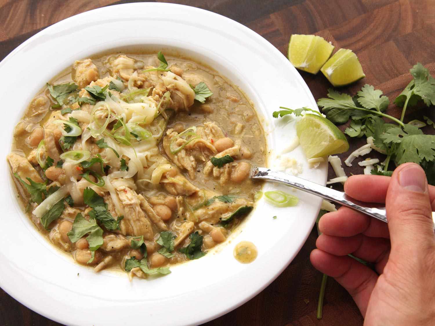 Hand lifting a spoonful of white chicken chili from a bowl.