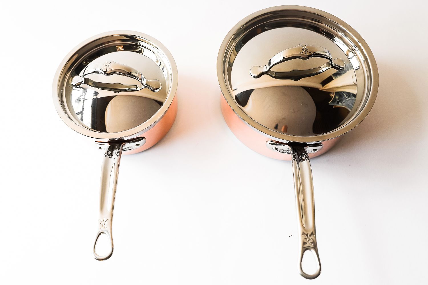 Two saucepans with lids side by side on a white background