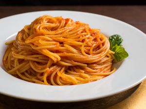 A serving of spaghetti that has been lightly coated with tomato sauce and fashioned into a swirl-like heap in a shallow bowl.