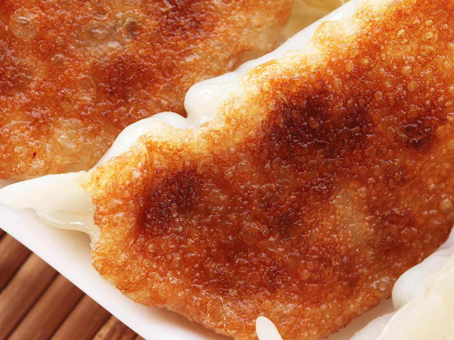 A close up of the bottom of a twice-fried and steamed dumpling. The dumpling is golden brown with lots of crisp texture.
