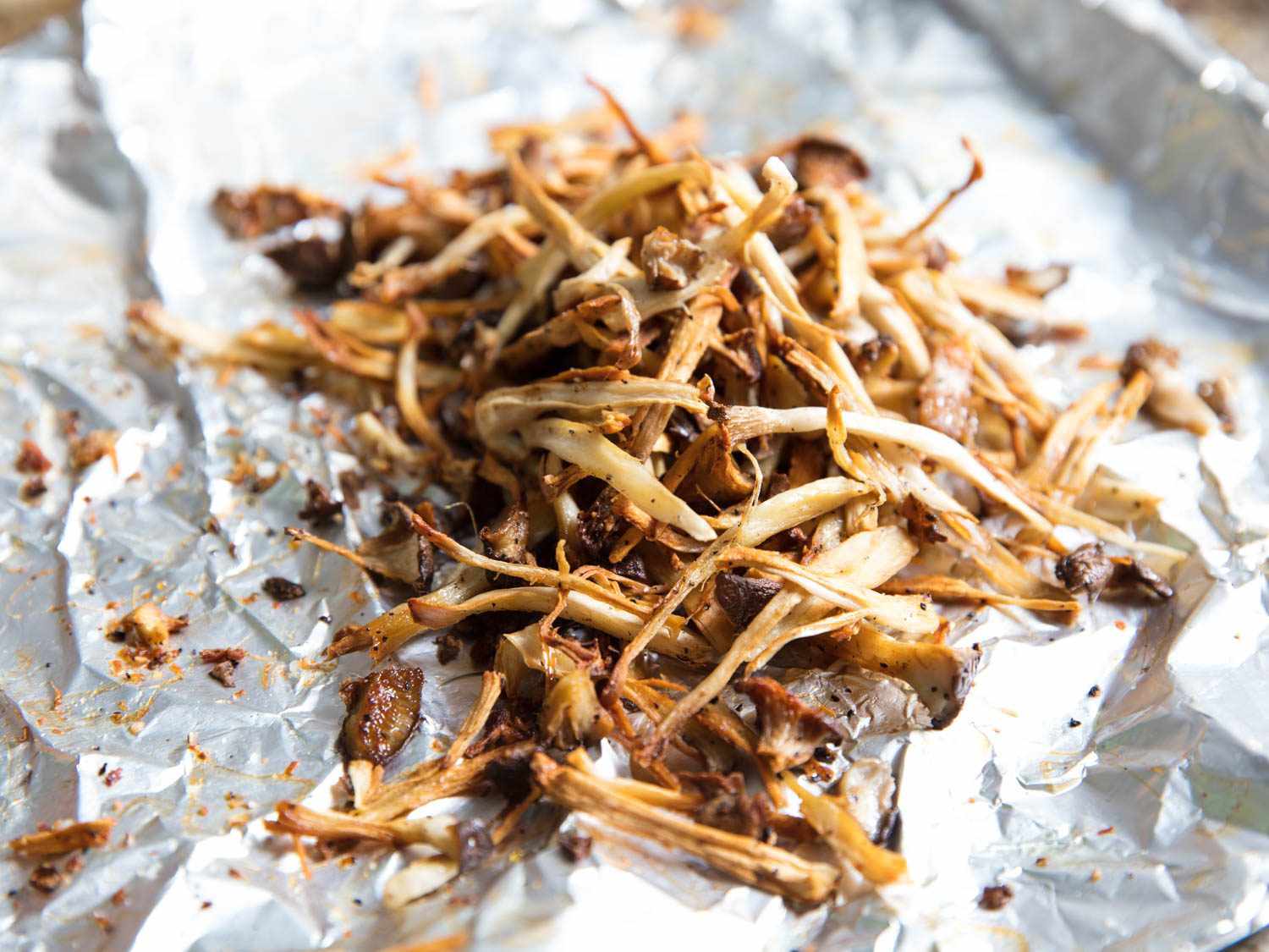 Browned and shredded king oyster mushrooms on aluminum foil.