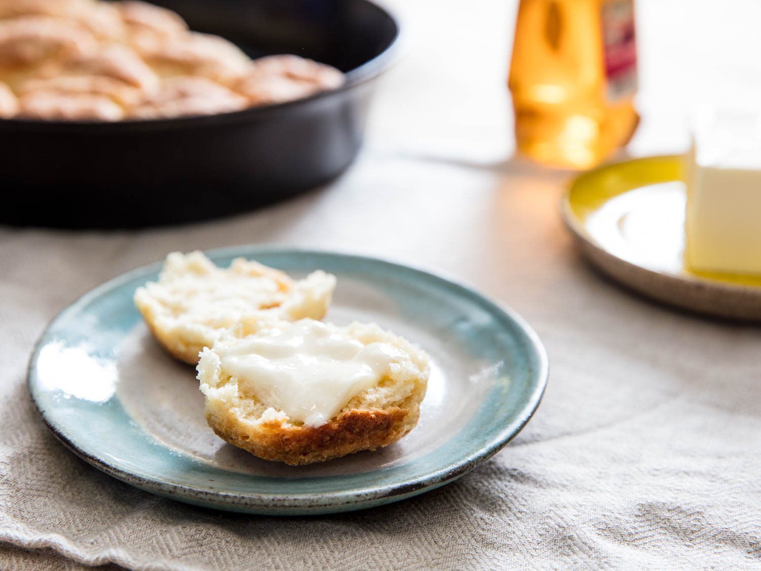Close up of a yogurt biscuit split open, slathered with butter.