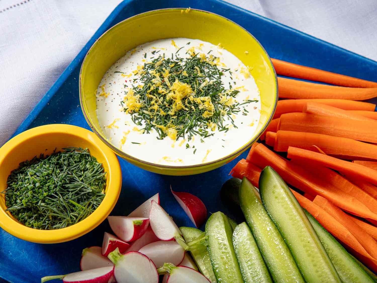 Whipped cottage cheese in a bowl with fresh herbs and lemon zest. Raw vegetables on the side.