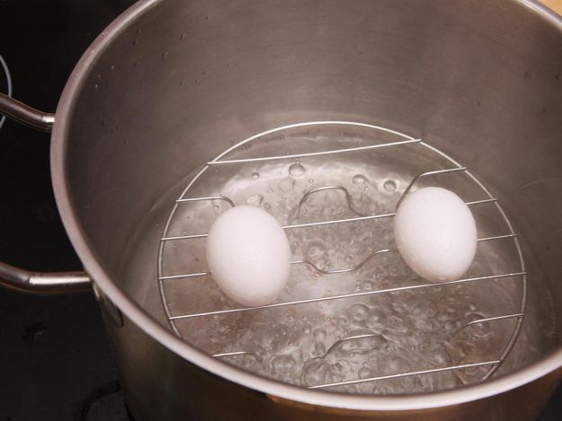 Two eggs resting on top of a steamer insert in a pot with boiling water.