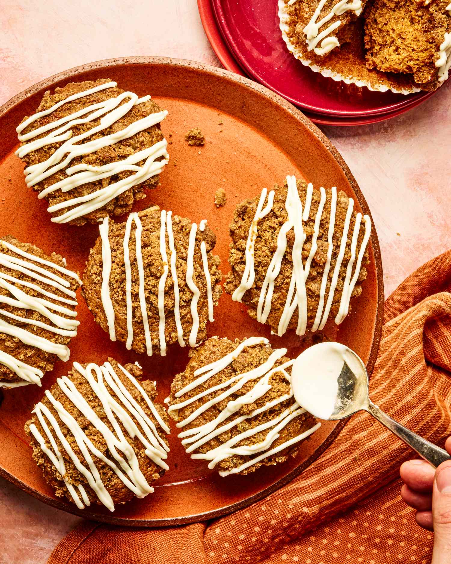 Gingerbread muffins topped with a white drizzle on a platter hand holding a spoon nearby