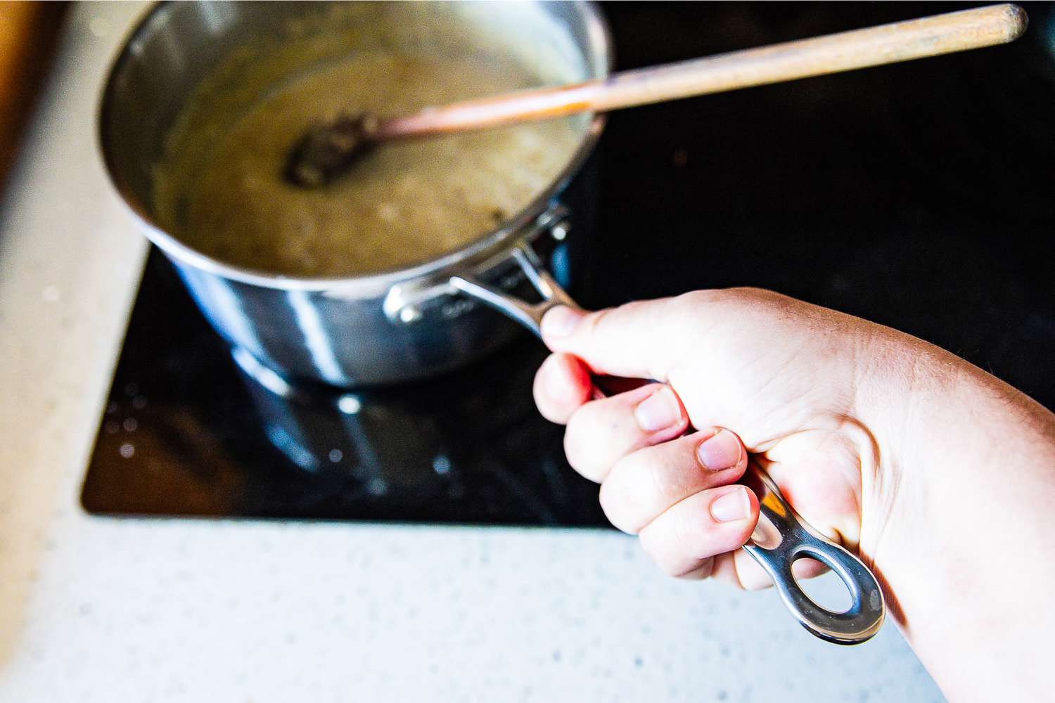 A hand holding the handle of a pot from the Goldilocks 7-piece Cookware Set