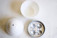 All of the parts of the Nordic Ware Egg Boiler on a white surface